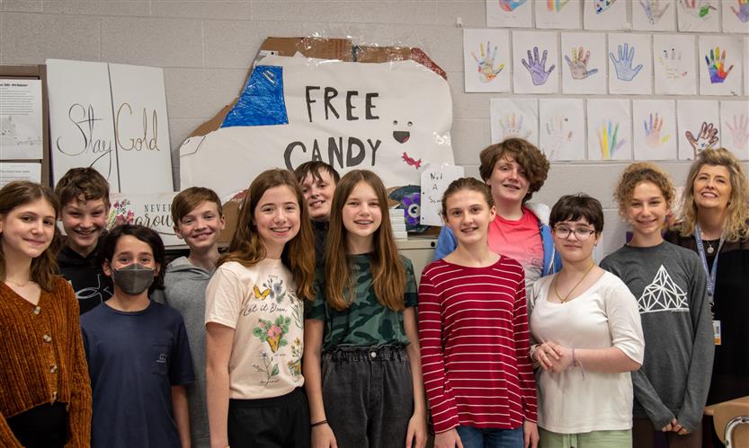 A group of sixth grade students stands in a school hallway.